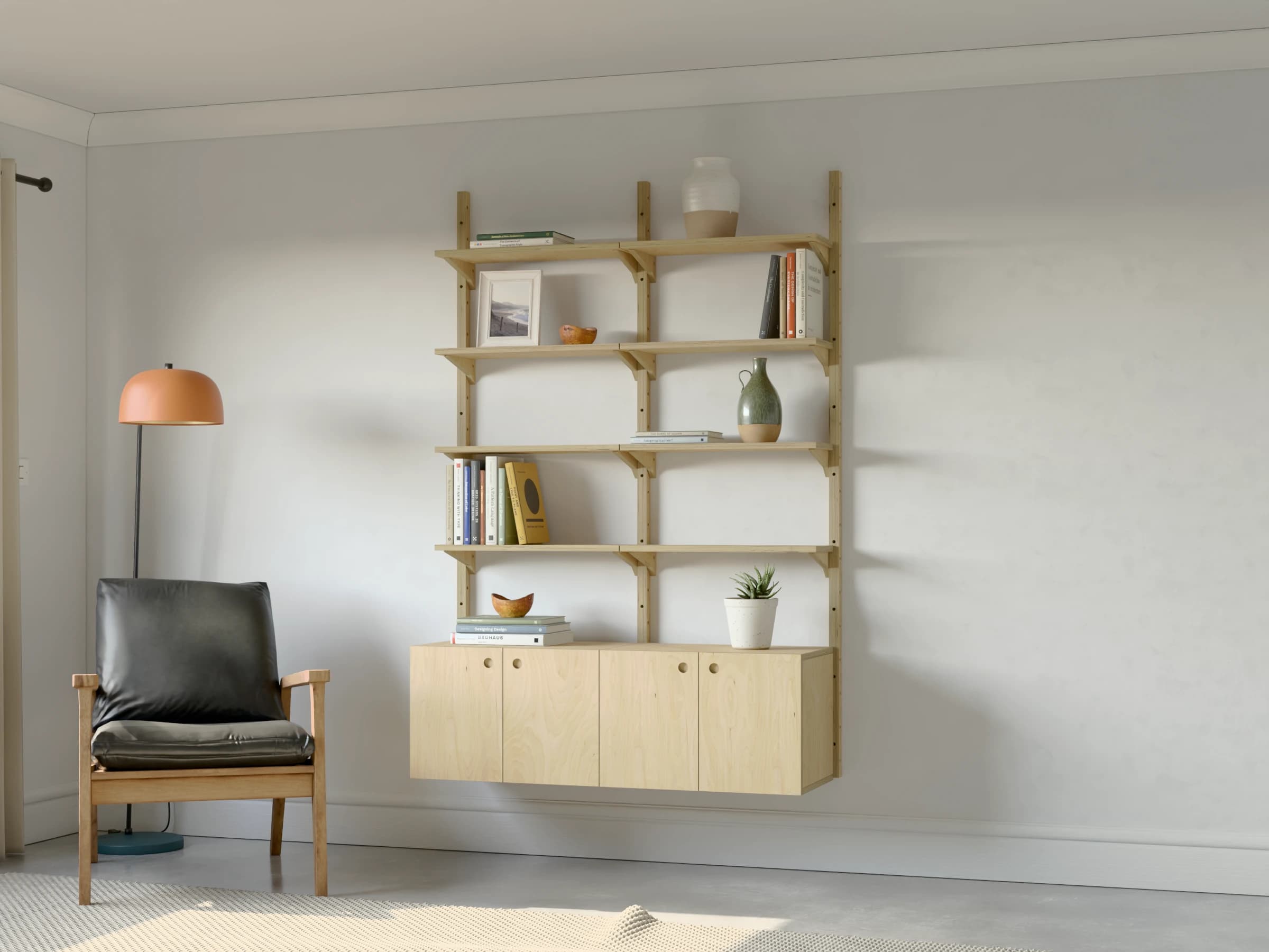 Two bays of birch plywood shelving with a two-door cupboard in each bay, styled with books and ceramics beside an armchair and a floor lamp